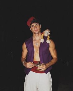 a man in white pants and a purple vest is holding a small stuffed animal on his chest