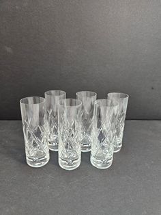 six crystal tumblers are lined up on a gray tablecloth, with one empty glass in the middle