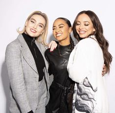 three women standing next to each other in front of a white wall with one woman smiling