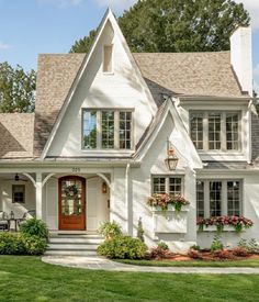 a white house with lots of windows and flowers in the front yard, along with green grass