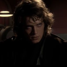 a man with long hair and blue eyes in a dark room looking at the camera