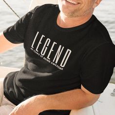 a man sitting on the back of a boat wearing a legend t - shirt that says, it's all sailing awesome