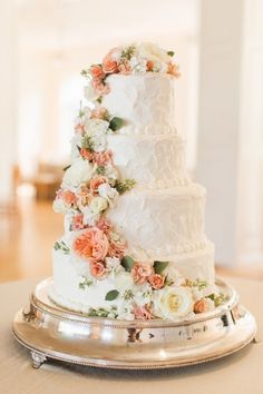 a three tiered wedding cake with flowers on the top and bottom is sitting on a silver platter