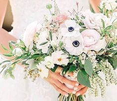 a bride holding a bouquet of white and pink flowers with greenery in her hands