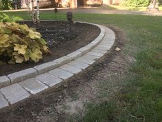 a brick garden edging in the middle of a yard with green grass and trees