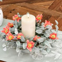 a white candle sitting on top of a table next to some flowers and greenery