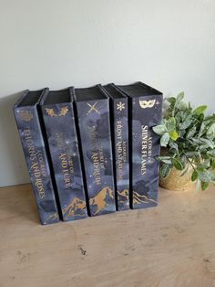 four books sitting on top of a wooden table next to a potted plant