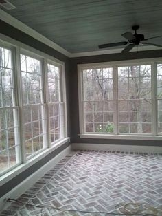 an empty room with three windows and brick flooring on the walls, along with a ceiling fan