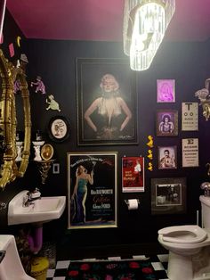 a bathroom decorated in black and white with pictures on the wall, toilet, sink and chandelier