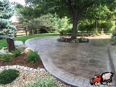 a large concrete patio surrounded by trees and landscaping materials in the back yard, with an orange truck parked on the driveway