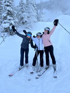 three people on skis standing in the snow with their arms up and hands raised