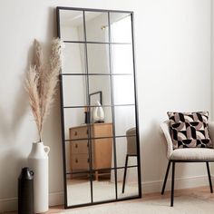 a mirror sitting on top of a wooden floor next to a white vase and chair