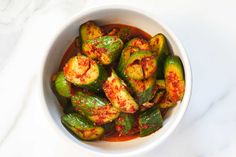 a white bowl filled with cooked zucchini and tomato sauce on top of a marble counter