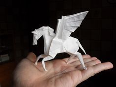 a hand holding a white origami horse