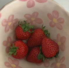 four strawberries in a white bowl with pink flowers