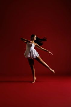 a woman in a white leotard is doing a dance move on a red background