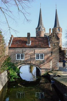 an old brick building with two towers next to a small river in front of it