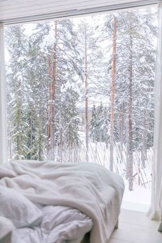 an unmade bed in front of a window with snow on the ground and trees outside