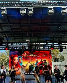 a group of people standing on top of a stage next to a giant screen with an advertisement behind them