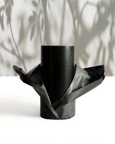 a black candle holder sitting on top of a white table next to a leafy plant