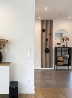 a white room with a black vase on top of a table and a mirror behind it