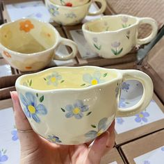 a hand holding a white and blue flowered tea cup in front of other cups