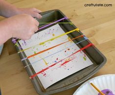 a child's hand is painting on a piece of paper with colored paint and sticks