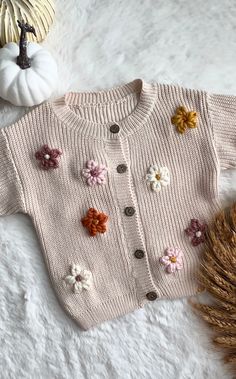 a knitted sweater with flowers on it next to a pumpkin and some dried grass