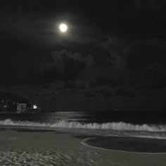 a full moon is seen over the ocean on a dark night with waves crashing in to shore