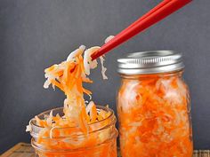 a spoon full of shredded carrots being held up by two jars with red chopsticks