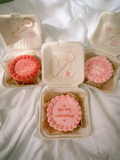 three pink cupcakes in plastic containers on a bed