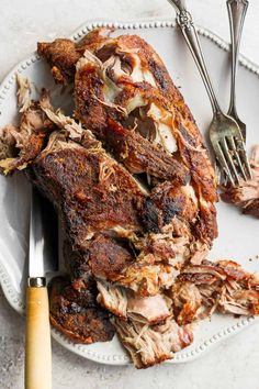 a white plate topped with meat next to a knife and fork