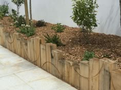 a wooden planter filled with lots of plants next to a white wall and stone floor