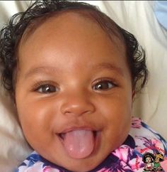 a close up of a baby laying on a bed with its tongue out and eyes wide open