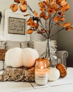 pumpkins and candles on a table in front of a white couch with an orange flower