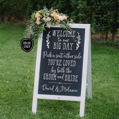 a chalkboard sign with flowers and greenery on it for an outdoor wedding ceremony