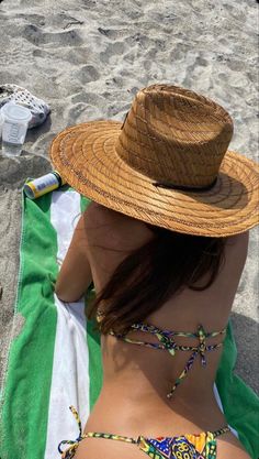 a woman laying on top of a beach next to a green and white striped towel