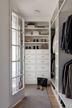 a walk - in closet with white cabinets and open doors, shoes on the floor