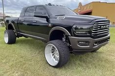 a large black truck parked on top of a grass covered field in front of a building