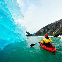 a person in a kayak paddling through an ice cave on the water near mountains