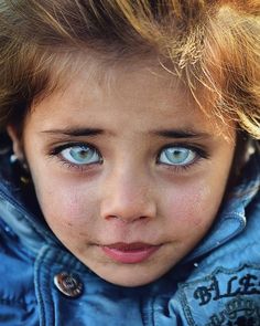 a close up of a child with blue eyes wearing a jacket and looking at the camera