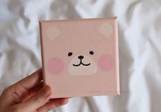 a hand holding up a pink square with a bear face painted on it's side