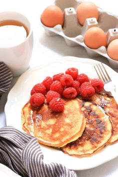 pancakes with raspberries are on a plate next to some eggs and a cup of coffee