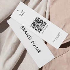 two white business cards sitting on top of a tan shirt with qr code printed on it