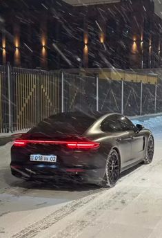 a black sports car driving down a snow covered street in the dark night with its rear lights on