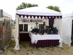 an outdoor tent set up with items for sale on the table in front of it