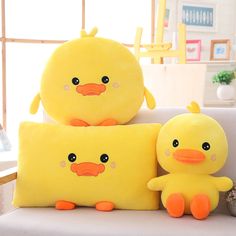 two yellow stuffed ducks sitting next to each other on a white couch in front of a window