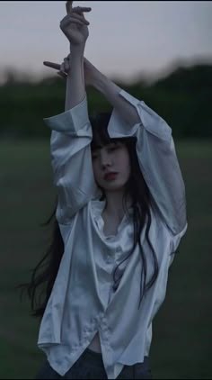 a woman in white shirt and black skirt holding her arms up with both hands while standing on grass field