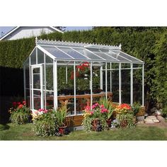 a small greenhouse with potted plants and flowers in the ground next to some bushes