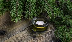 a candle is lit in a glass bowl on a wooden table surrounded by pine branches